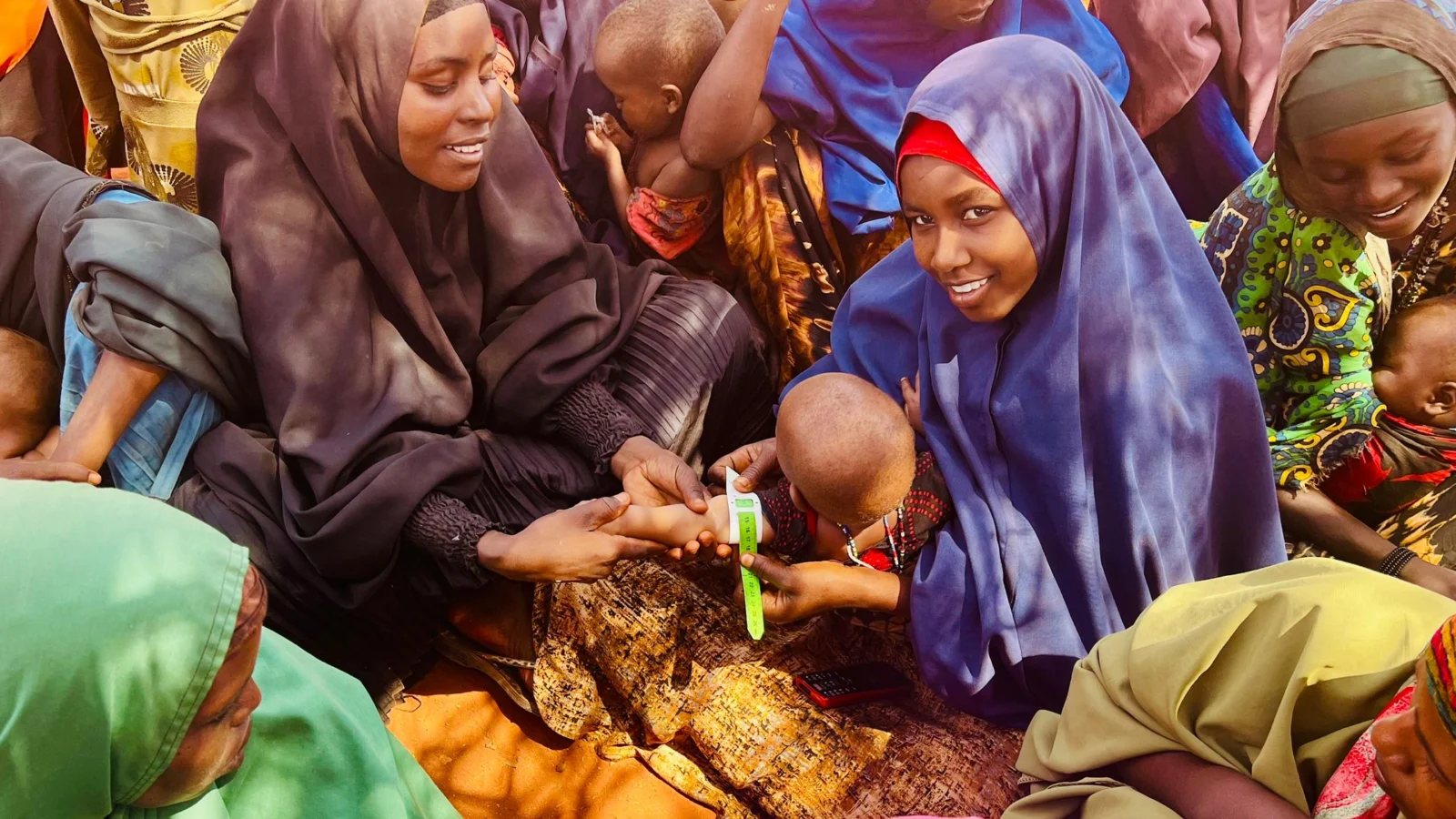 Mothers and young children at a nutrition screening, where a MUAC band is measured around a baby's arm