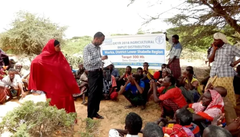 BADEF staff addressing families seated outdoors at a cash and agricultural input distribution in Marka District